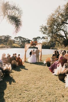 A romantic outdoor wedding ceremony by the lake on a sunny day with guests seated.