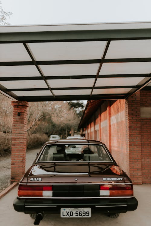 Free A classic brown car parked beneath a garage awning with a city street backdrop. Stock Photo