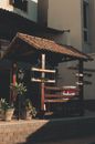 Little wooden kiosque with brown tiled roof and flowerpots near residential house on sunny day