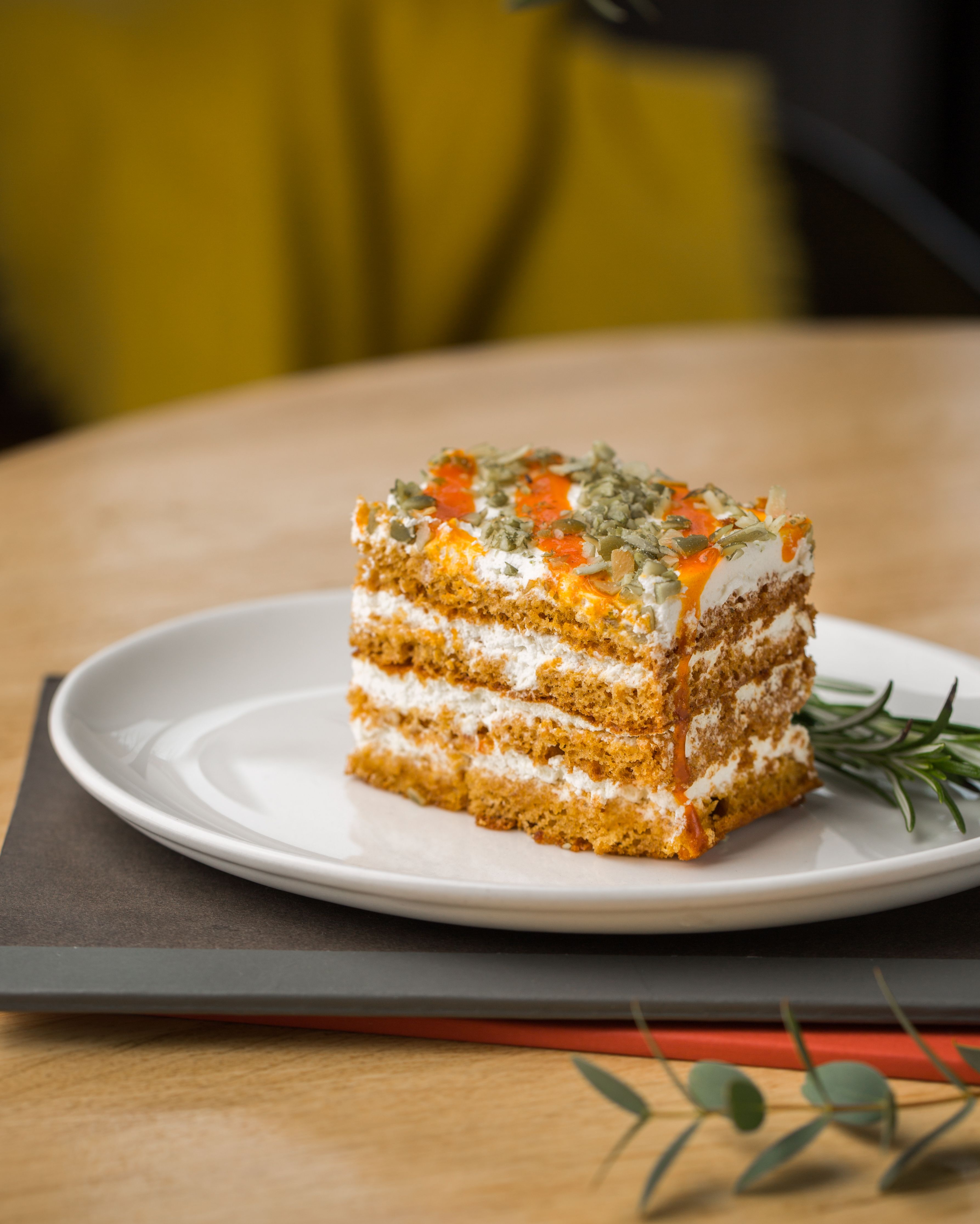 Close-up of a layered carrot cake slice topped with cream and seeds.