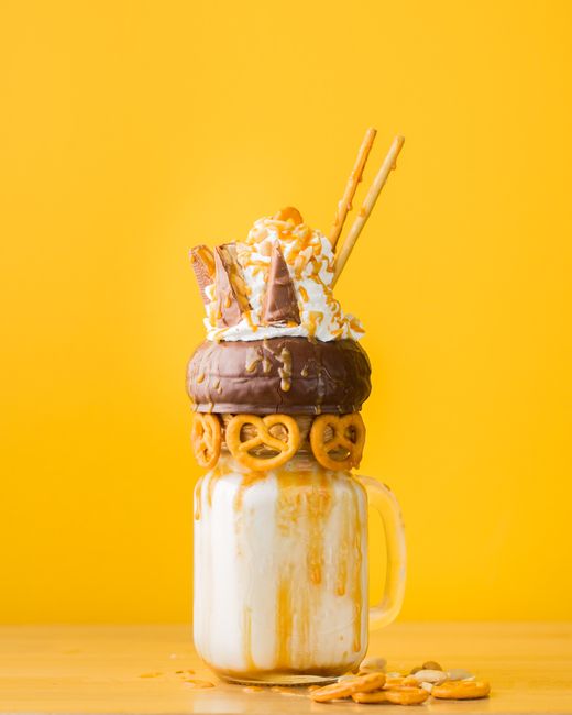 Delicious milkshake with donuts, pretzels, and chocolates set against a yellow background.