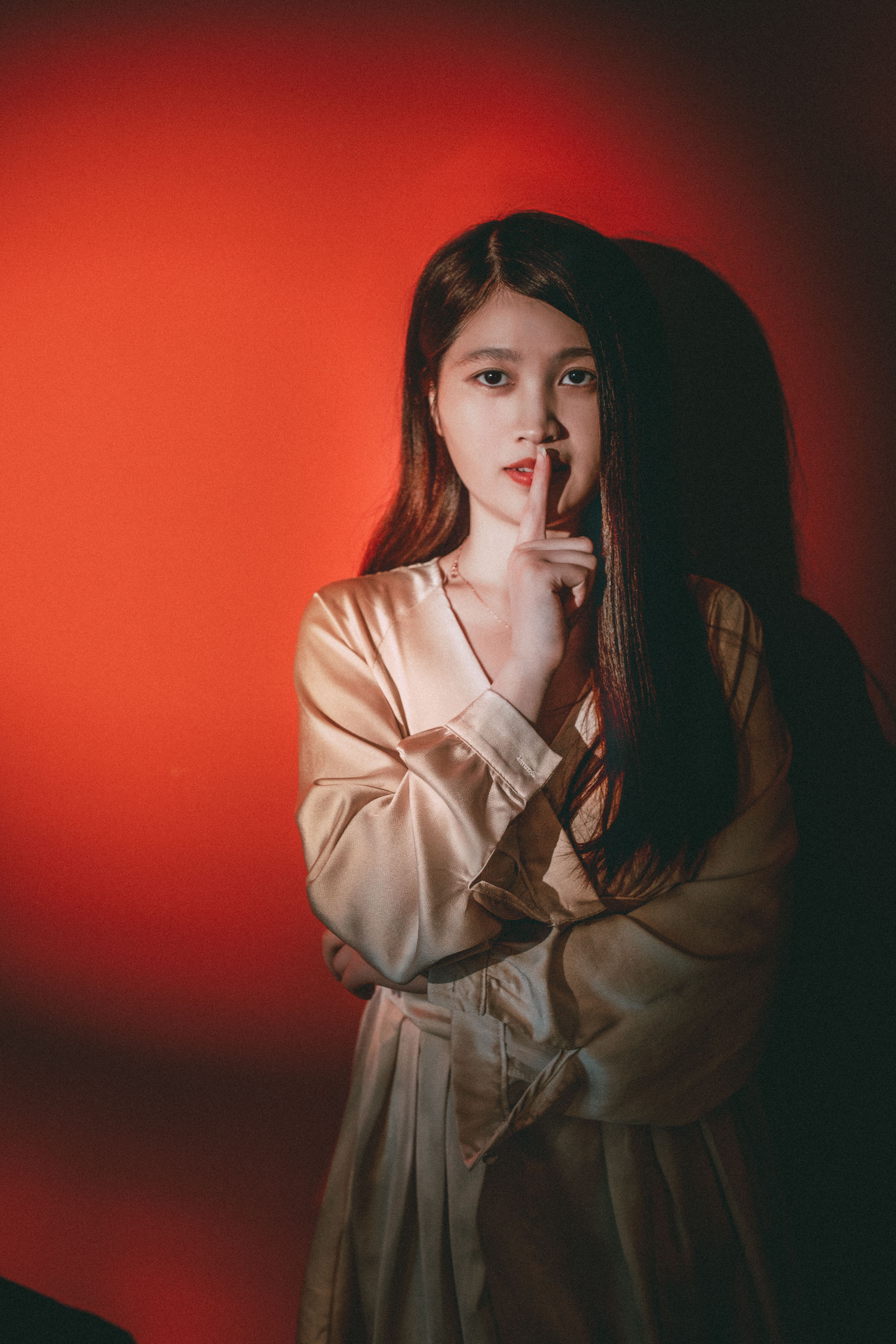 Stylish portrait of a woman posing with finger on lips in a studio setting with red background.