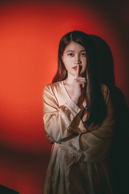Stylish portrait of a woman posing with finger on lips in a studio setting with red background.