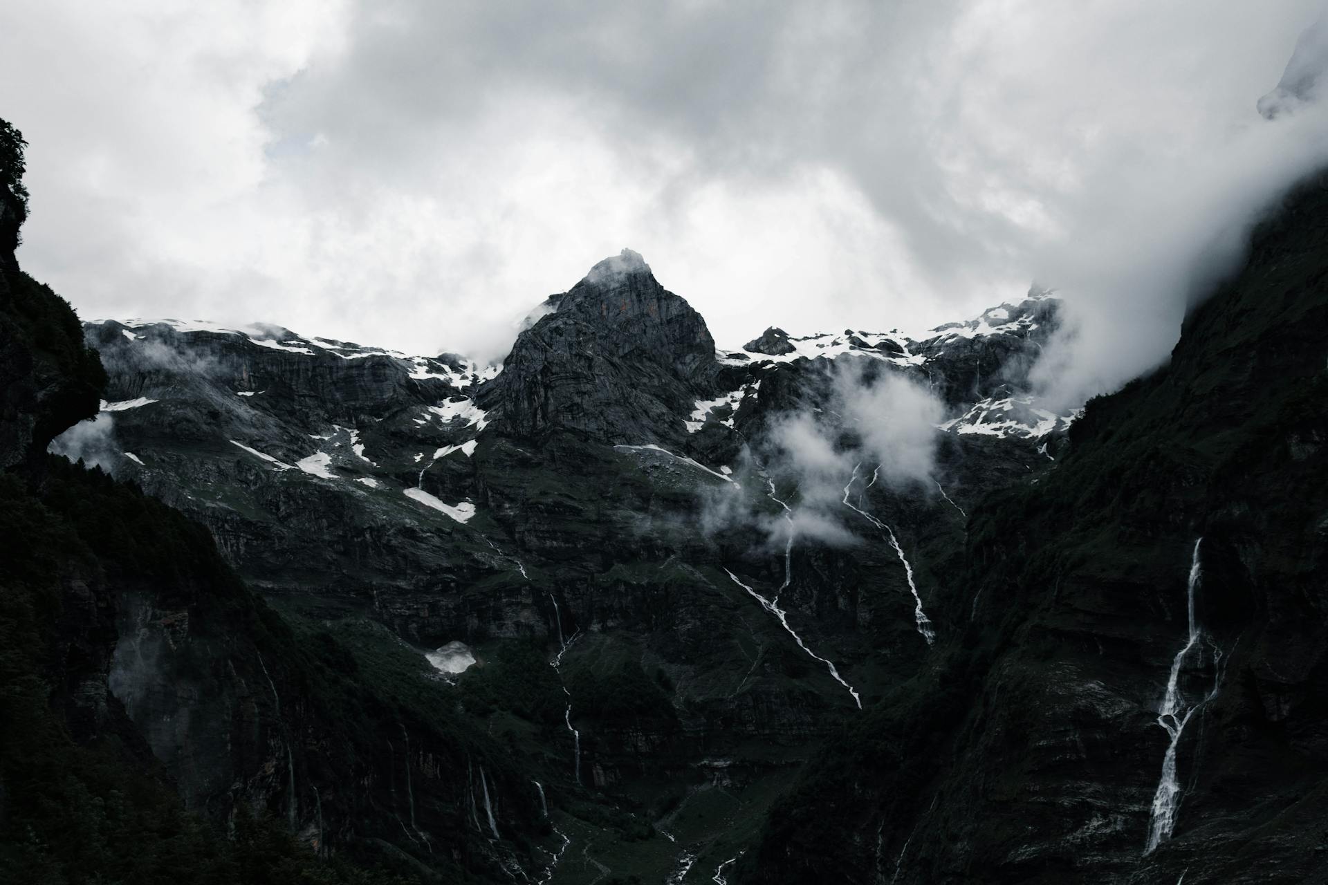 Majestic mountain peaks at Sixt-Fer-à-Cheval shrouded in clouds, revealing rugged beauty in a dramatic nature scene.