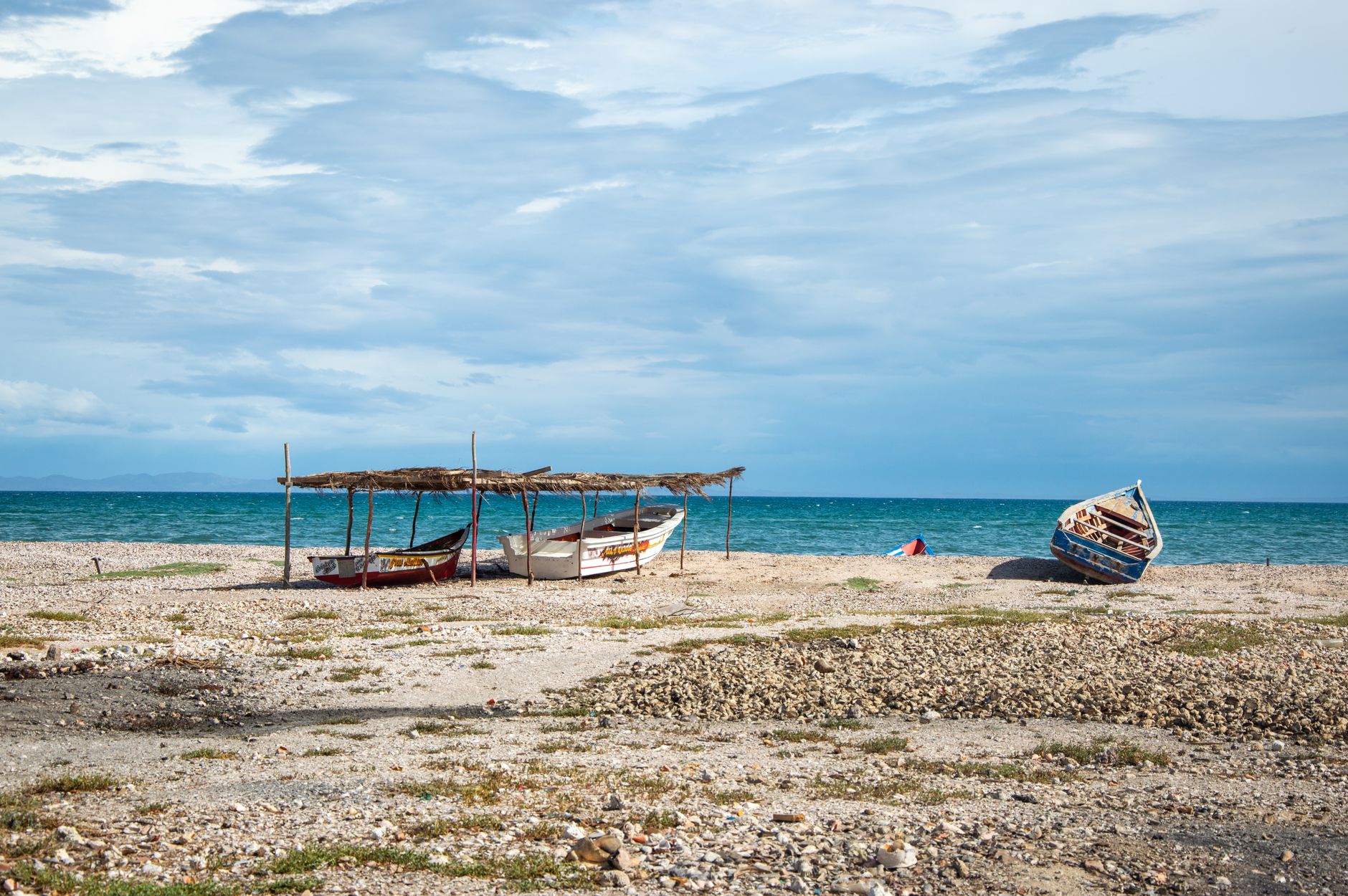 Serene beach with fishing boats and calm sea under a vast sky.
