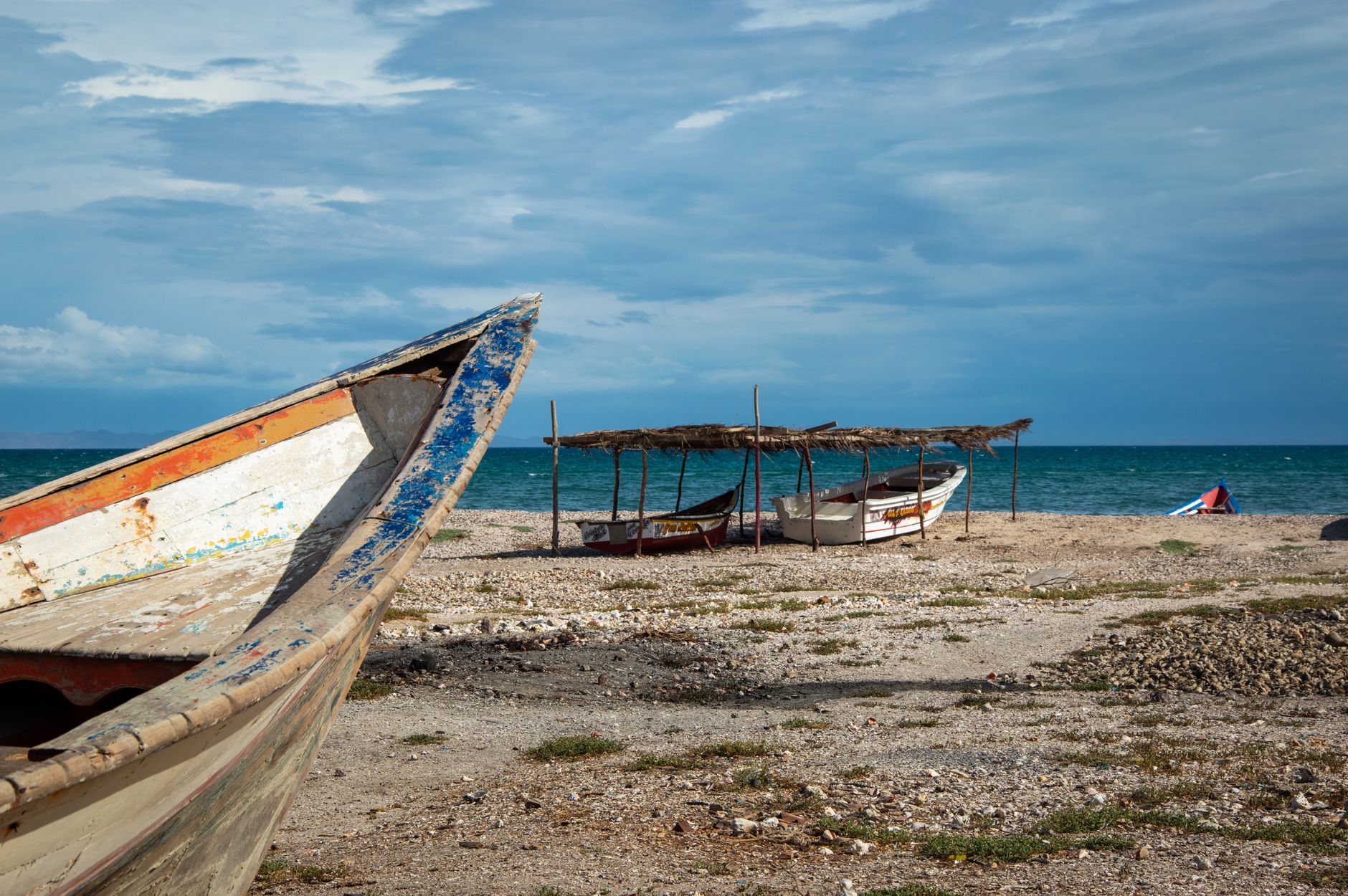Weathered fishing boats resting on a rocky beach by the sea under a cloudy sky.