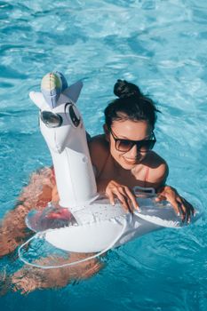 Woman smiling in a pool with a unicorn floatie, enjoying a sunny summer day.