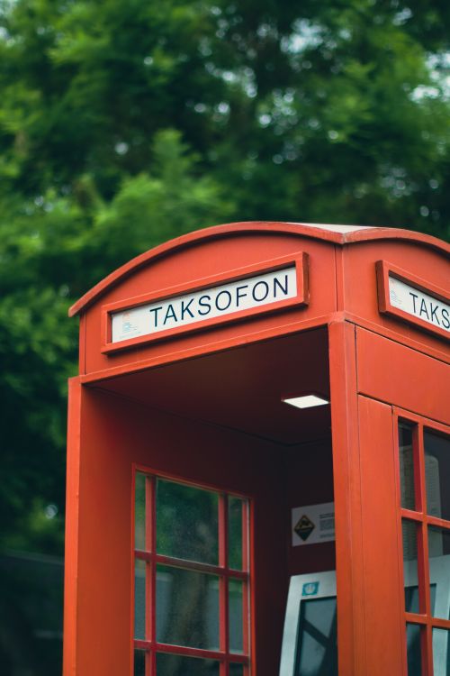 Free Classic red phone booth labeled 'Taksofon' in a lush green park atmosphere. Stock Photo