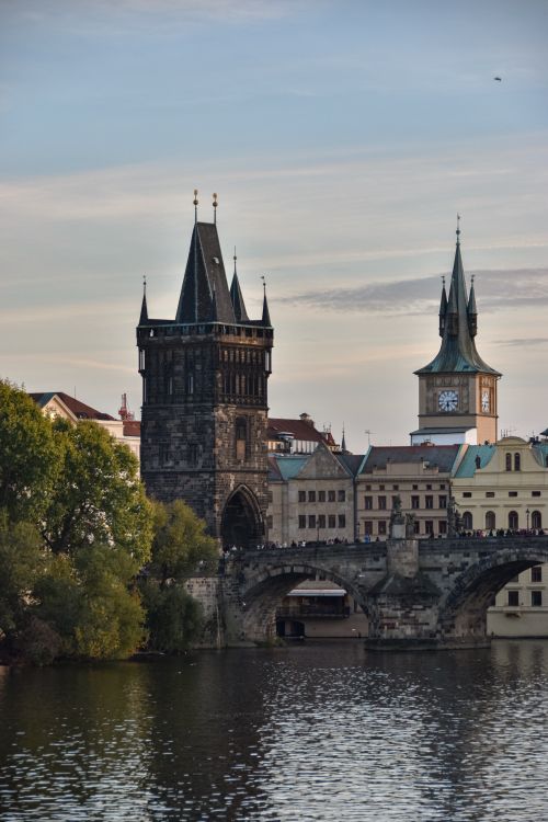 Free Iconic view of Charles Bridge in Prague, featuring historic towers and tranquil river scene at sunset. Stock Photo
