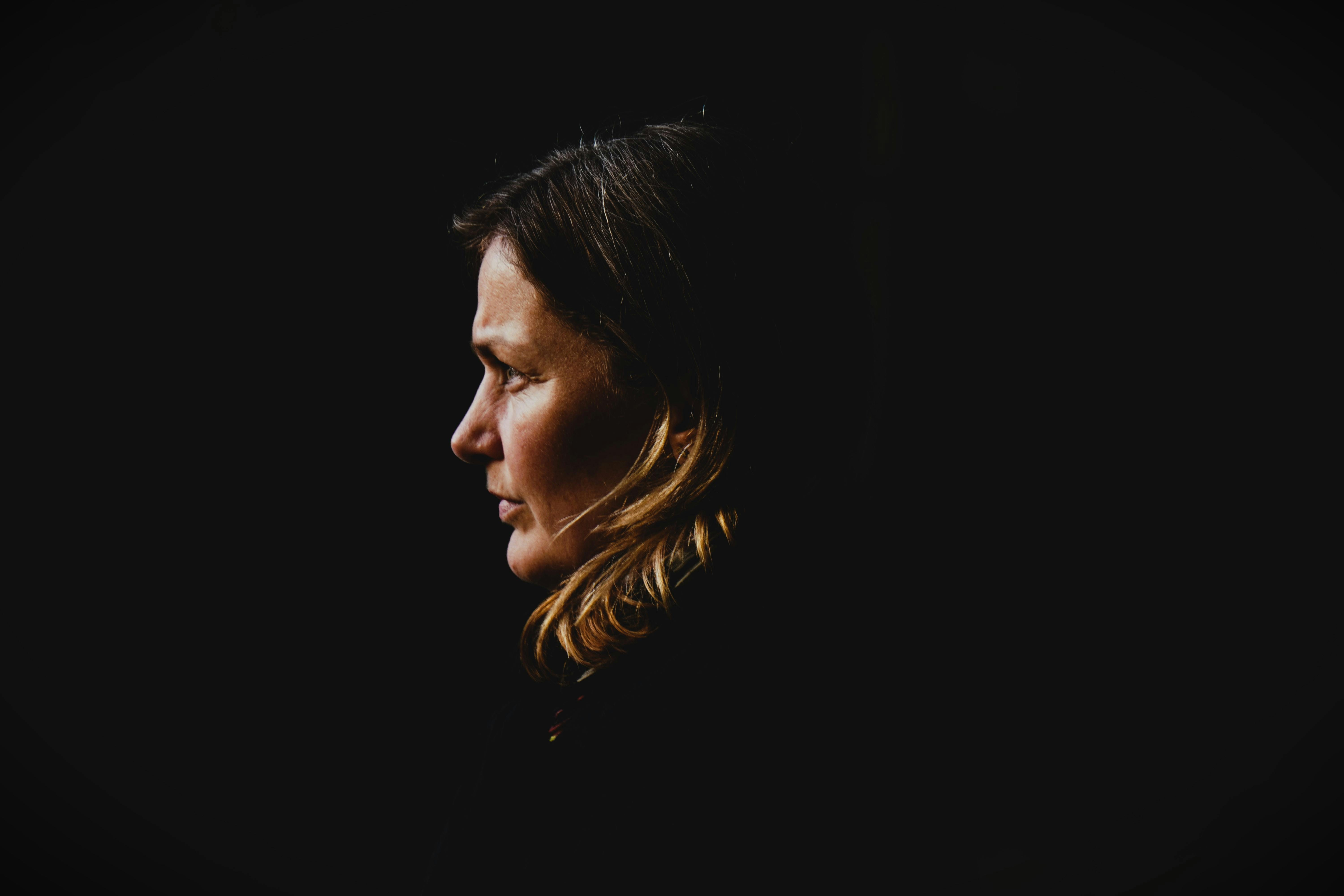 Side profile portrait of a woman with dark background, capturing introspection.