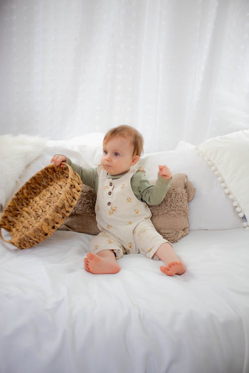 Free A baby sitting on a bed with a basket Stock Photo