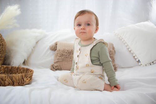Free A baby sitting on a bed wearing a white outfit Stock Photo