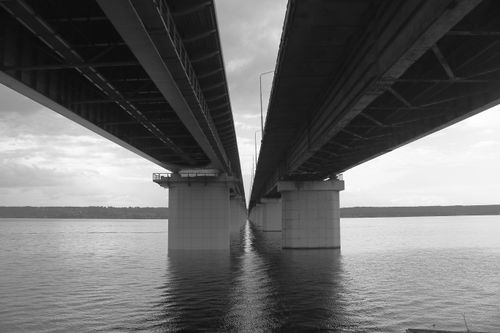 Free A modern bridge with a dramatic perspective over a calm river in black and white. Stock Photo
