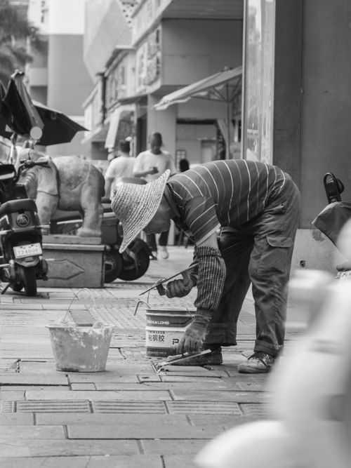 Free A focused worker spackles a city sidewalk in a black and white urban setting. Stock Photo