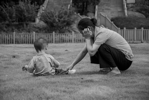 A mother and child enjoying a moment on the grass in a rural setting.