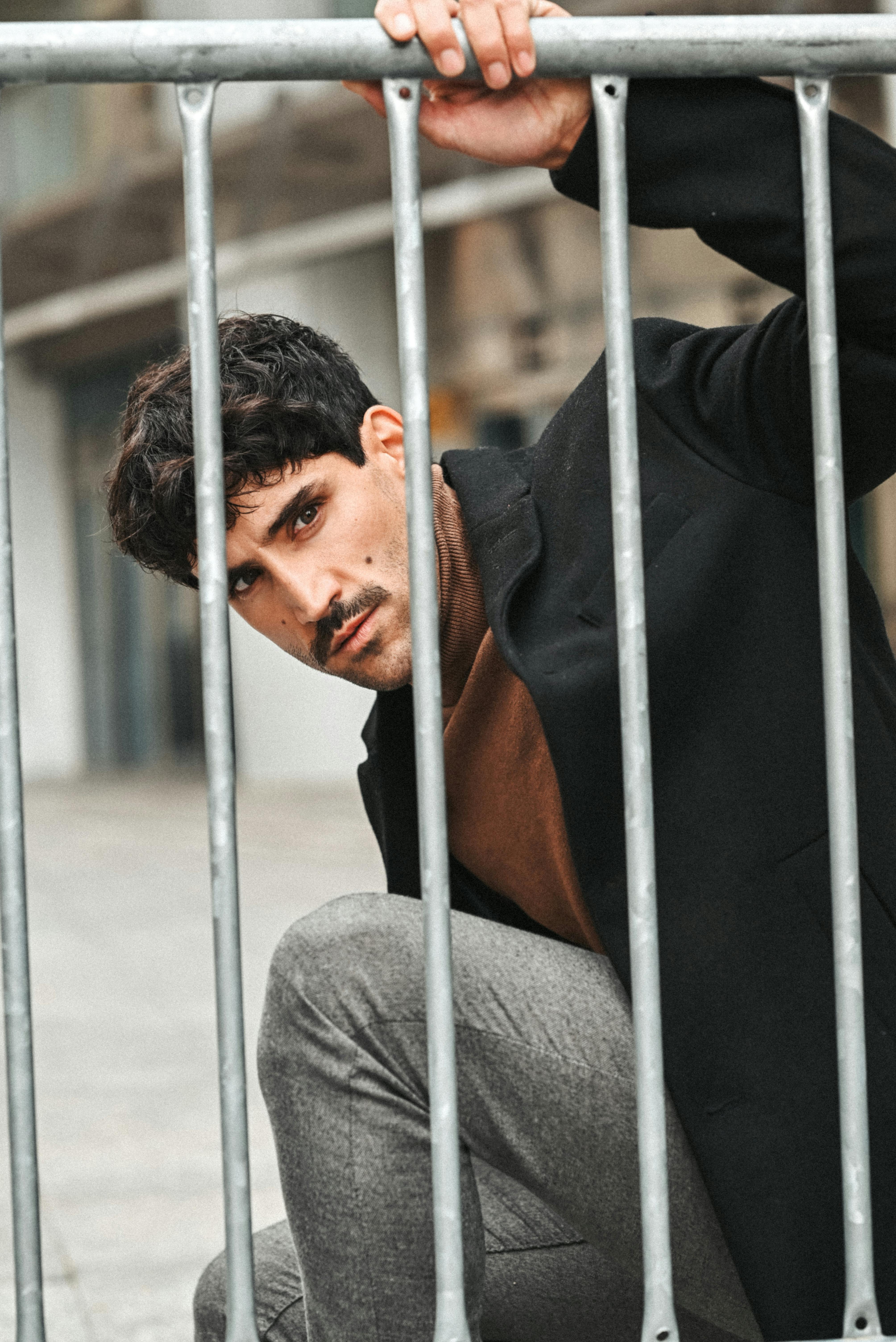 a fashionable man crouching behind a metal barrier