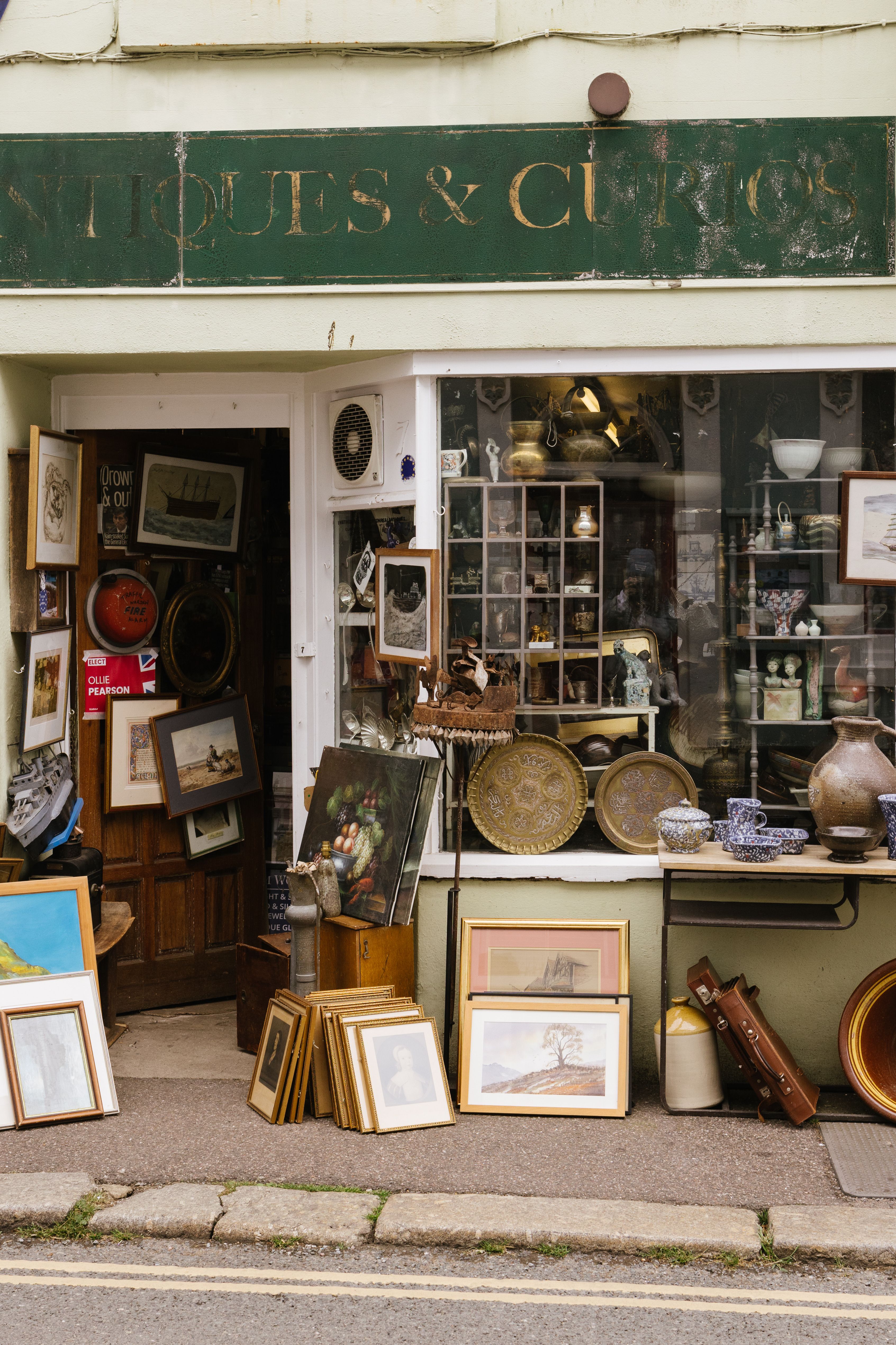 Explore a quaint antique shop entrance with vintage paintings, pottery, and curios on display.