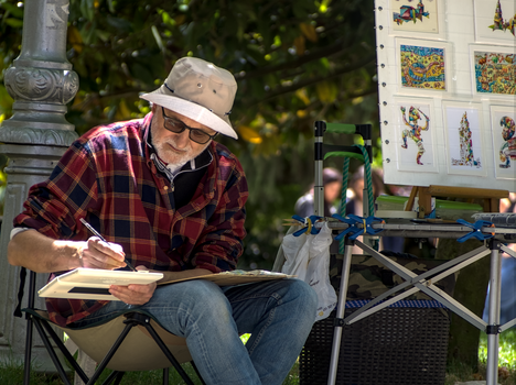 Elderly man sketching in a park in Santiago de Compostela, Spain, under sunny skies.