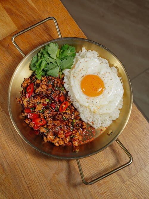 A bowl of rice, meat and an egg on a wooden table