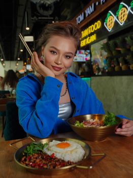 Smiling young woman with chopsticks enjoying Asian food at a trendy restaurant.