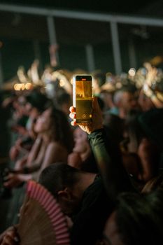 A lively concert audience capturing the performance on a smartphone. Vibrant atmosphere with focus on technology use.