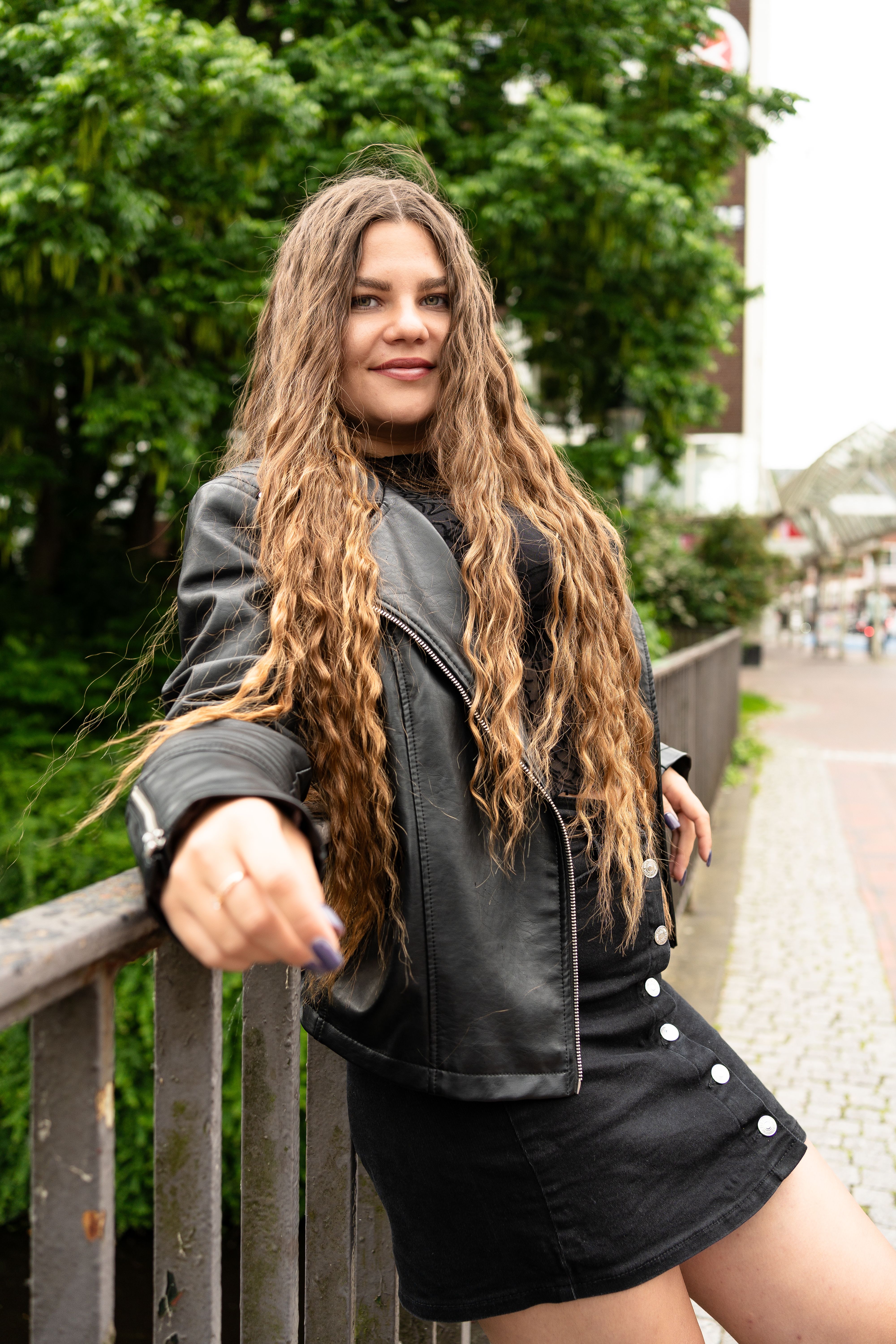 Fashionable woman with long hair wearing a black leather jacket and skirt outdoors in Emden, Germany.