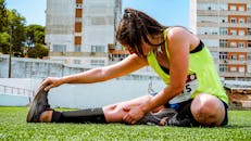 一名年轻女子穿着霓虹灯背心，在草地上伸展身体，为户外锻炼或跑步活动做准备