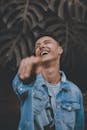 一名快乐的男子穿着牛仔夹克，笑着指指点点，周围是郁郁葱葱的绿色植物