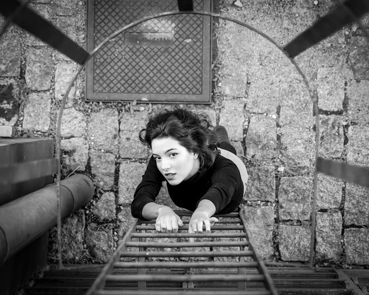 Gray Scale Photo Of A Woman About To Climb The Fire Escape Ladder