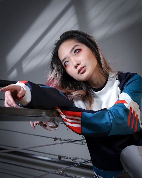 Free Young languid good looking Asian female with dyed hair and unusual makeup in trendy sweatshirt leaning on handrail and looking away Stock Photo