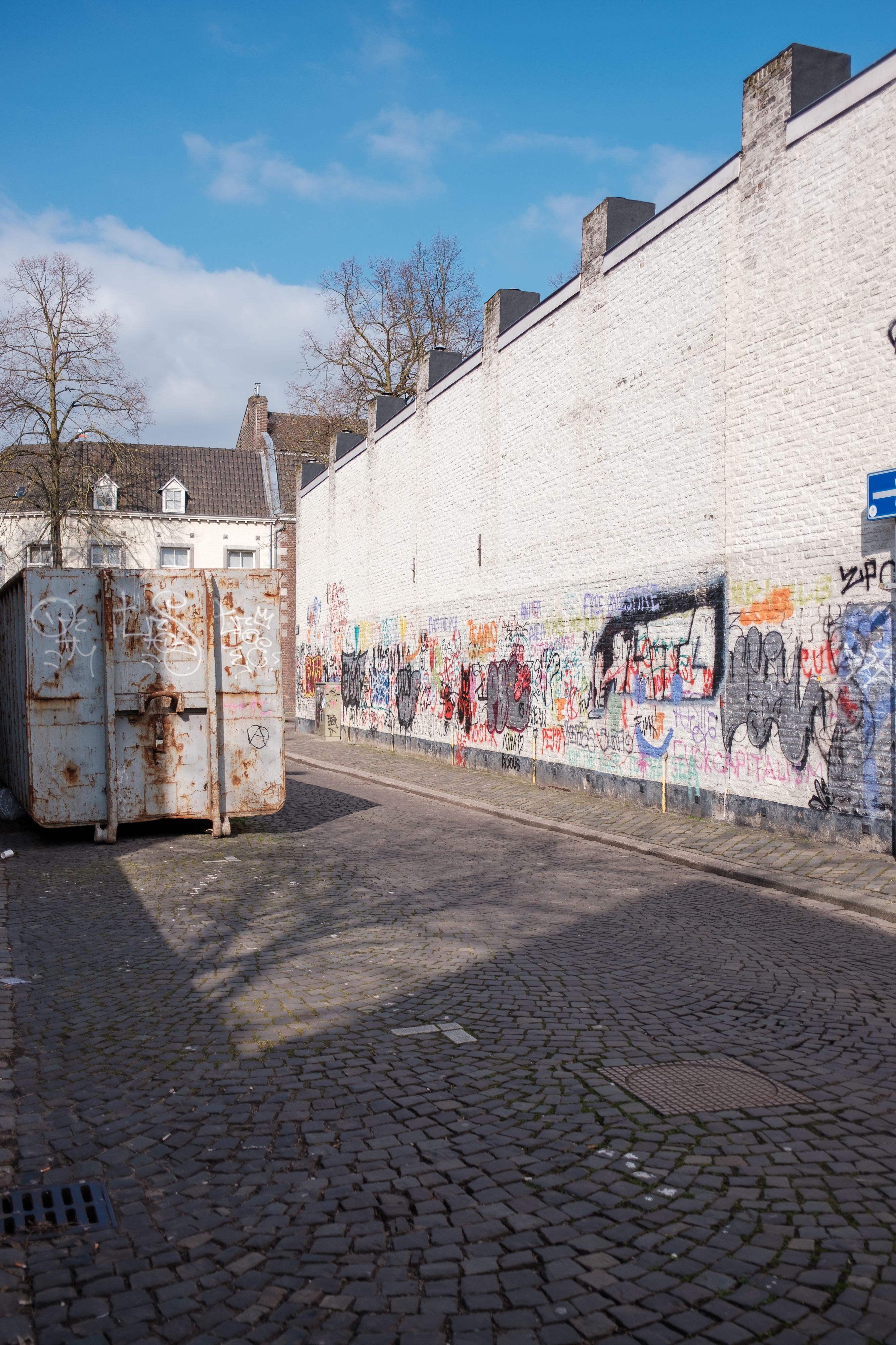 Colorful graffiti on a white brick wall with cobblestone street and shipping container.