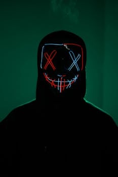 Mysterious figure with neon mask illuminated against a dark background.