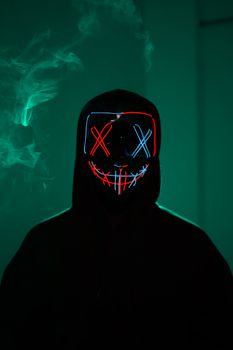 Dark portrait of a person wearing a neon LED mask in a mysterious atmosphere.
