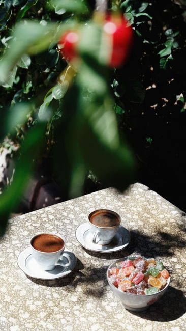Two cups of Turkish coffee and a bowl of colorful delights set on an outdoor table.