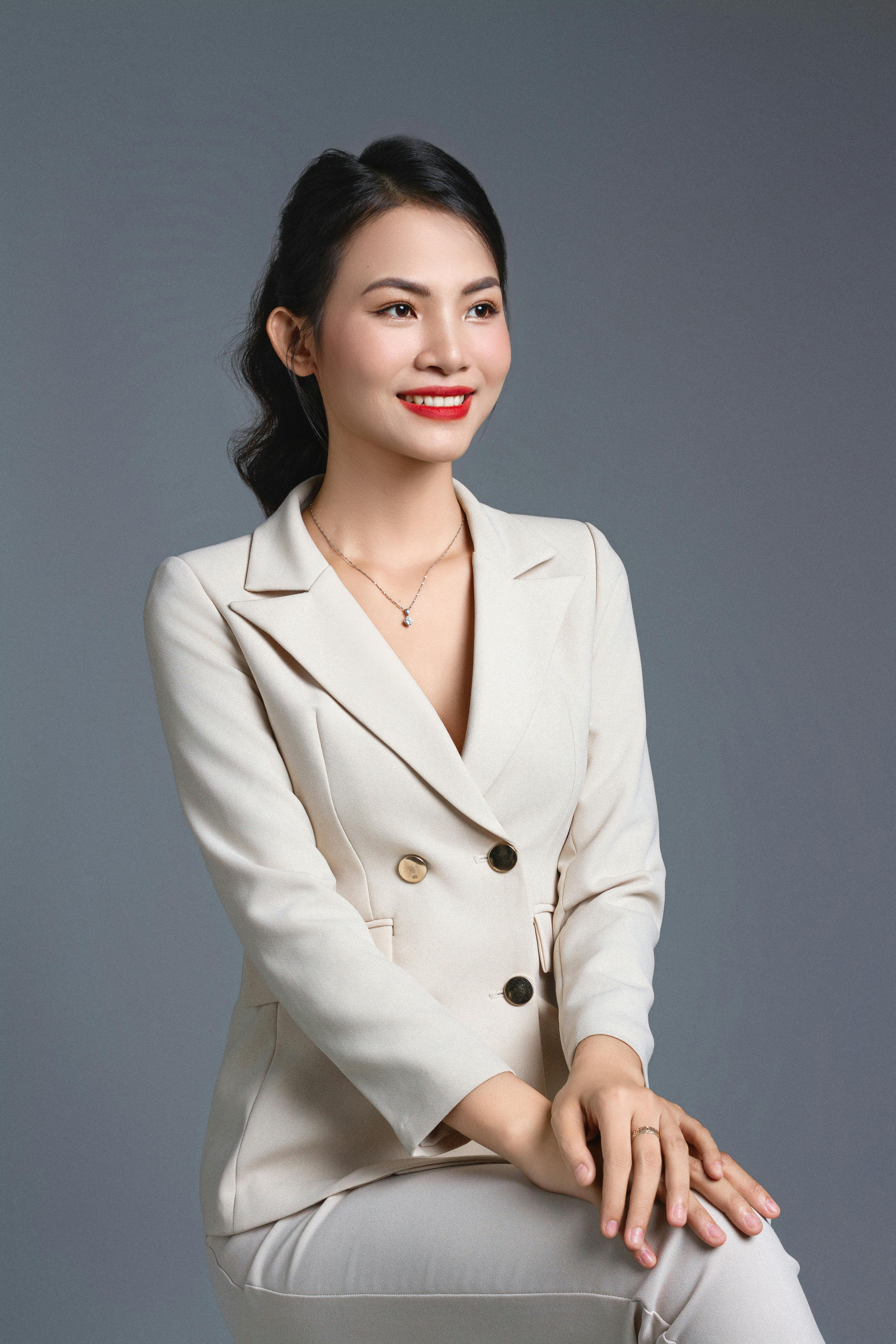 Elegant woman in a white suit, smiling and posing in a studio setting, showcasing modern fashion.