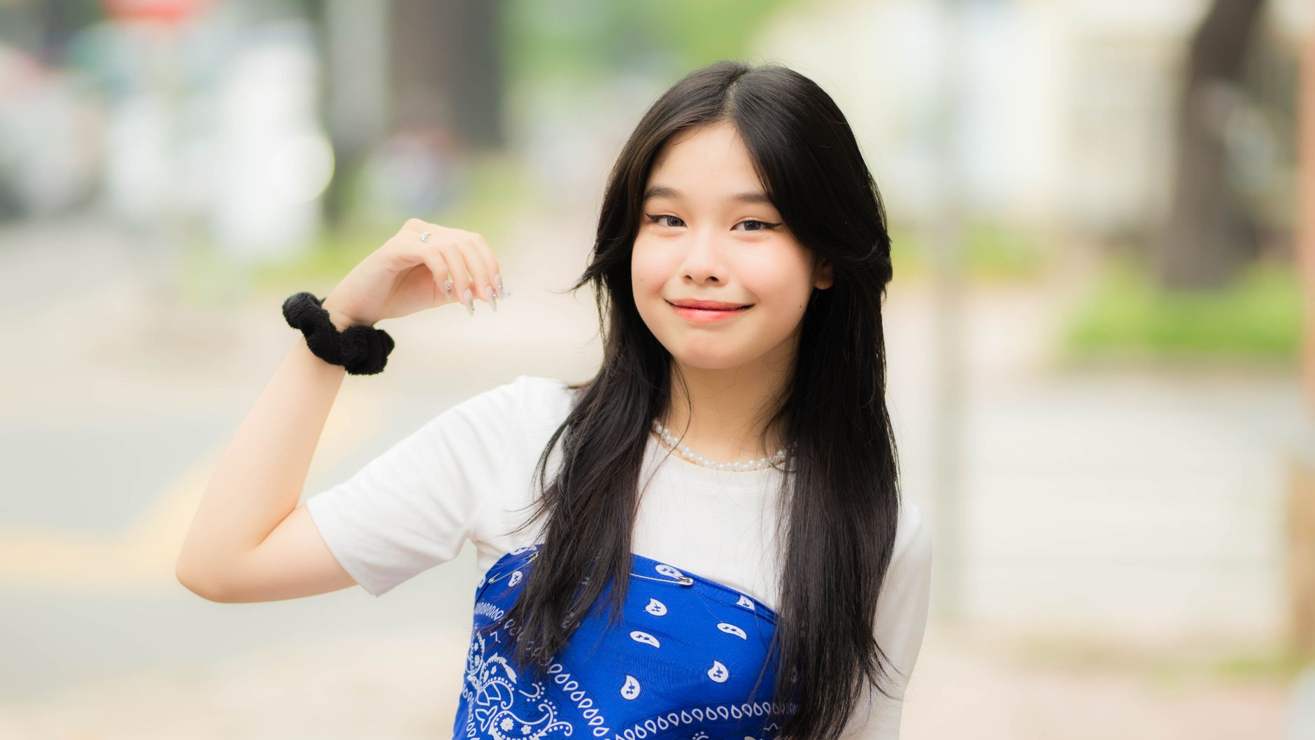 A young, smiling woman poses outdoors with a blue scarf, exuding charm and confidence.