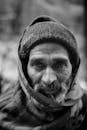 这是一幅黑白特写肖像，画面中的老人头戴无檐帽，颈系围巾，散发着温暖的气息