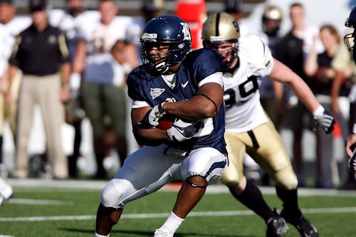 Football Player Hugging Ball While Opponent Chasing