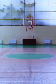Modern basketball court indoors with glass walls and wooden flooring. Ideal for sports facilities design.