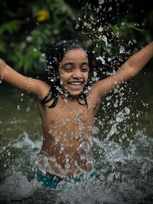 Free A happy child splashes water joyfully while playing in a river on a sunny day. Stock Photo
