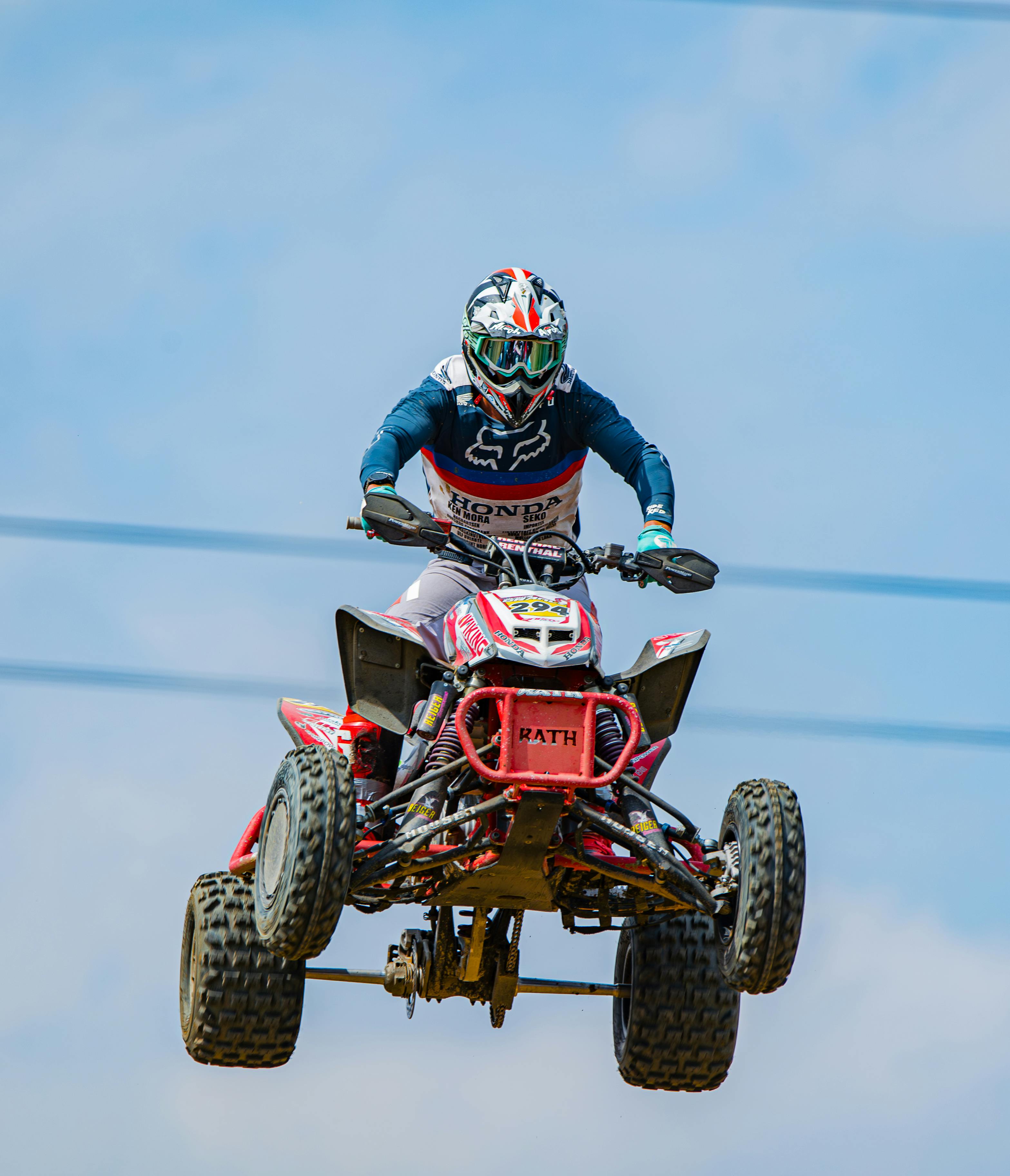 Racer airborne on a quad bike during a thrilling motocross competition on a clear day.