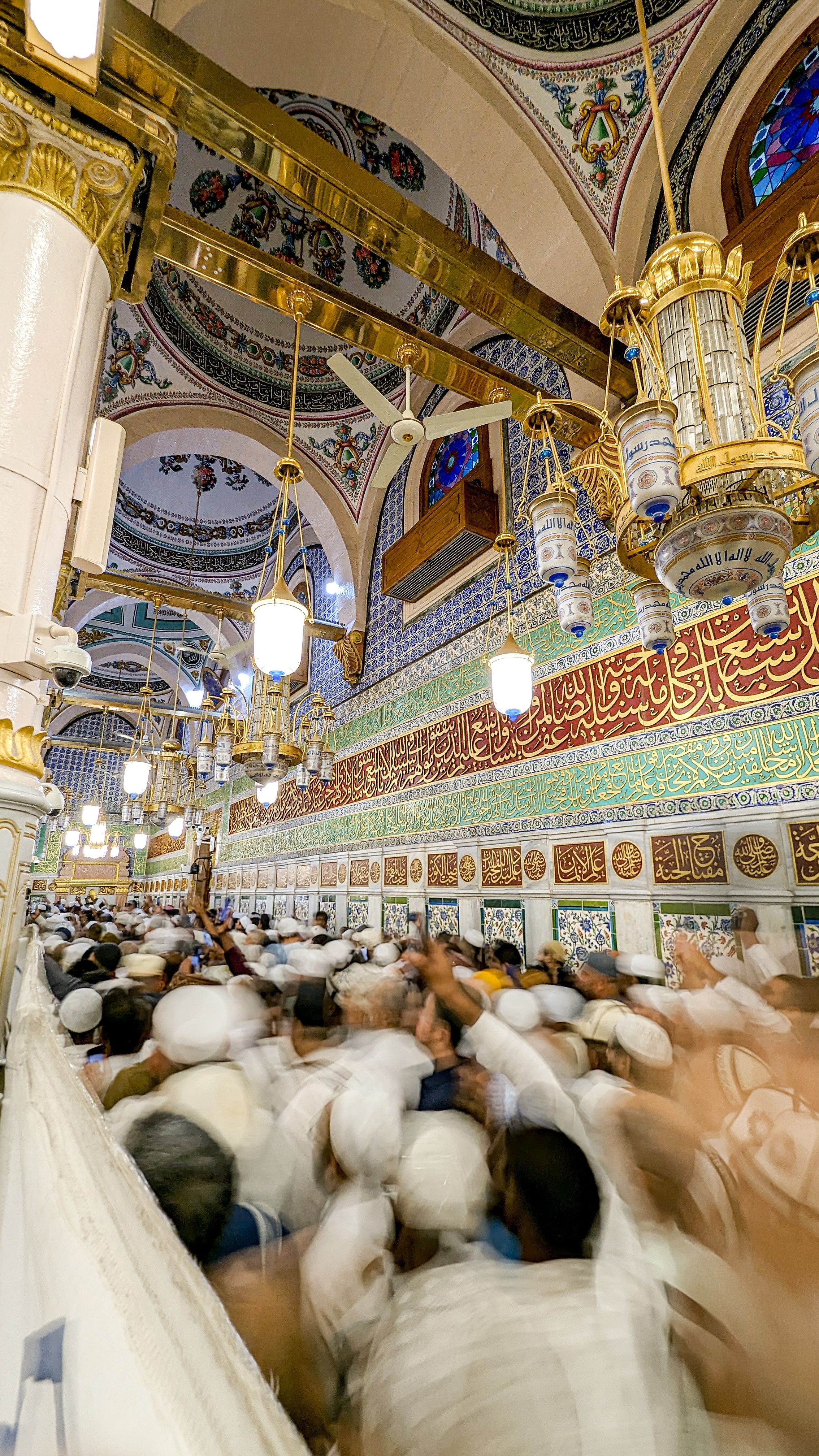 A crowded interior view of the Prophet's Mosque with detailed Islamic ornaments in Madinah, Saudi Arabia.