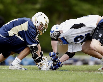 Two male athletes in a lacrosse faceoff during a competitive game on a grassy field.