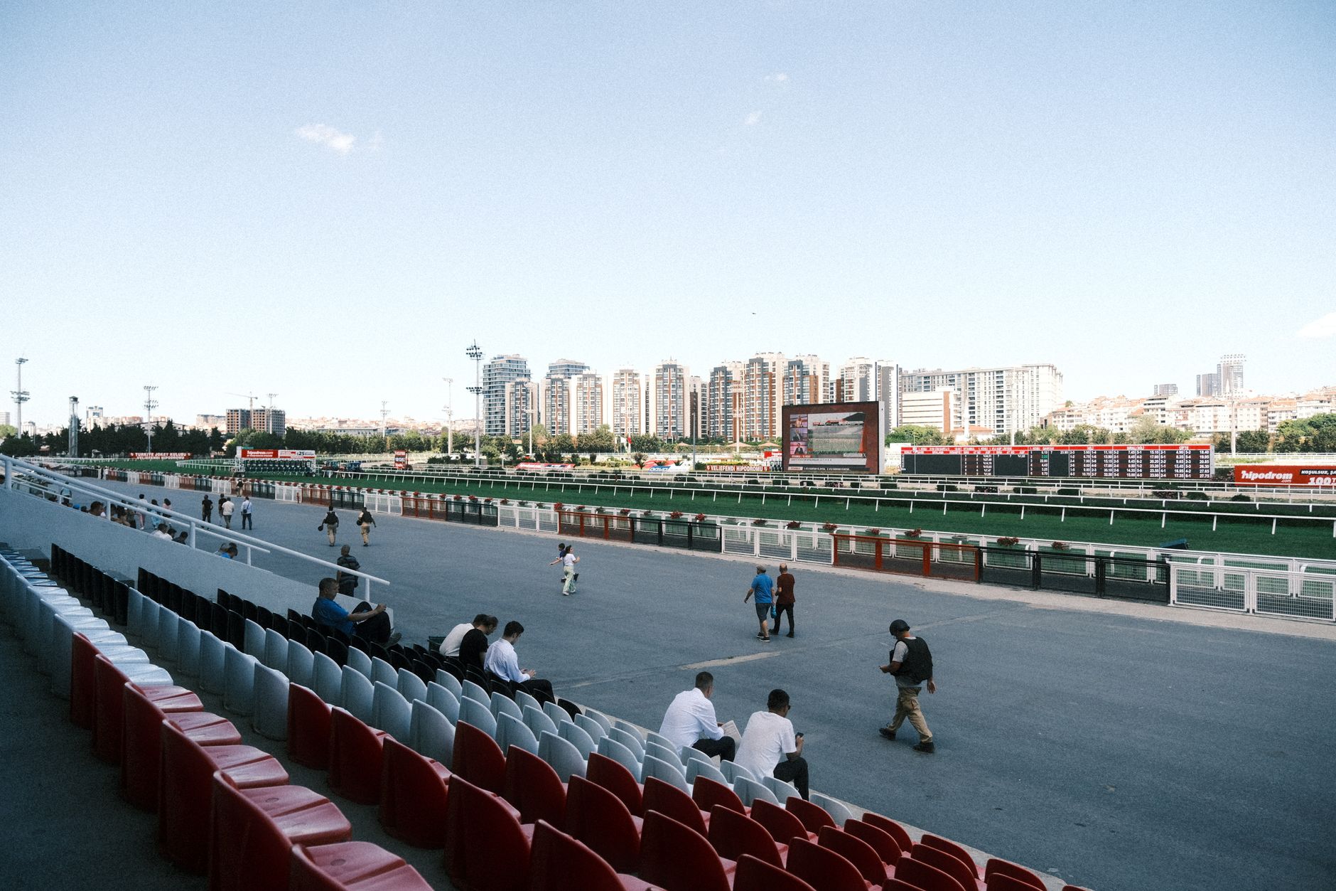 A serene race track with scattered spectators, urban skyline visible under bright daylight.