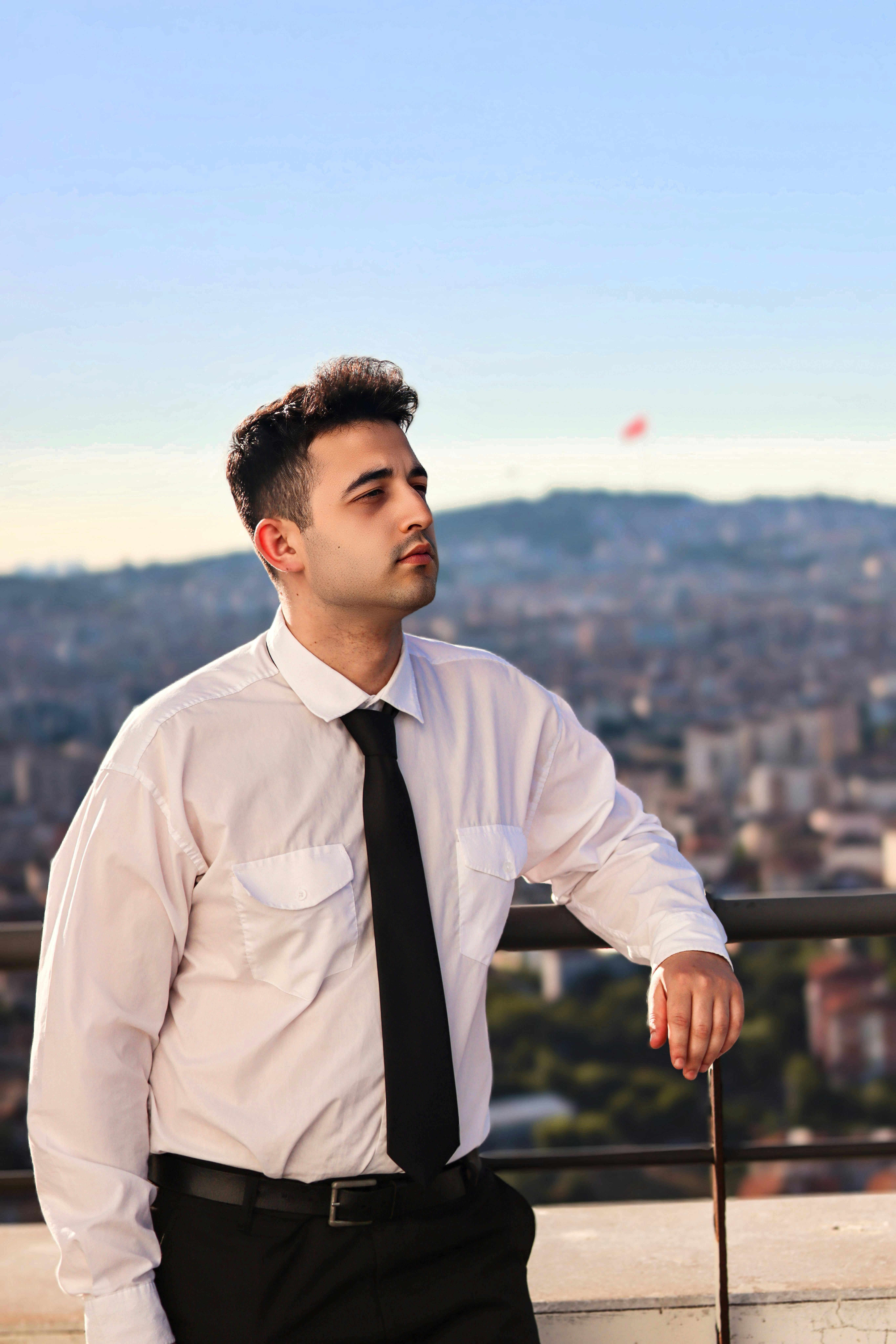 Young businessman in formal attire standing on a rooftop, overlooking the cityscape with a thoughtful expression.