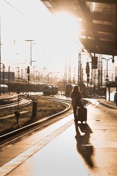 A traveler with a suitcase walks down a railway platform during sunset, casting a long shadow.