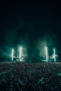A large crowd enjoys a dynamic night concert under bright stage lights and smoky effects.