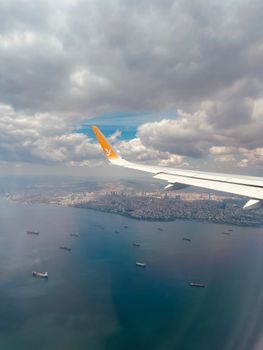 Stunning aerial view of a city along a coastline with an airplane wing and ships below.
