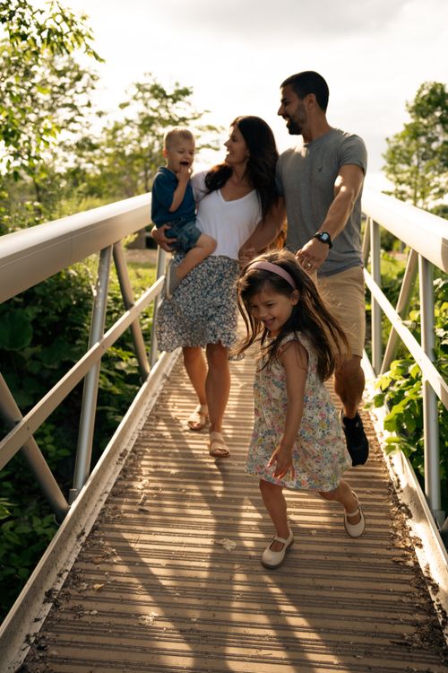Free Joyful family enjoying a sunny day walking on a footbridge surrounded by nature. Stock Photo
