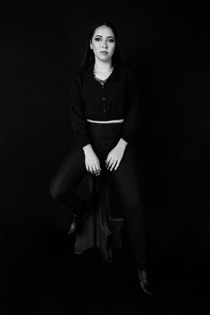 Black and white portrait of a woman in fashion attire, sitting gracefully in studio.